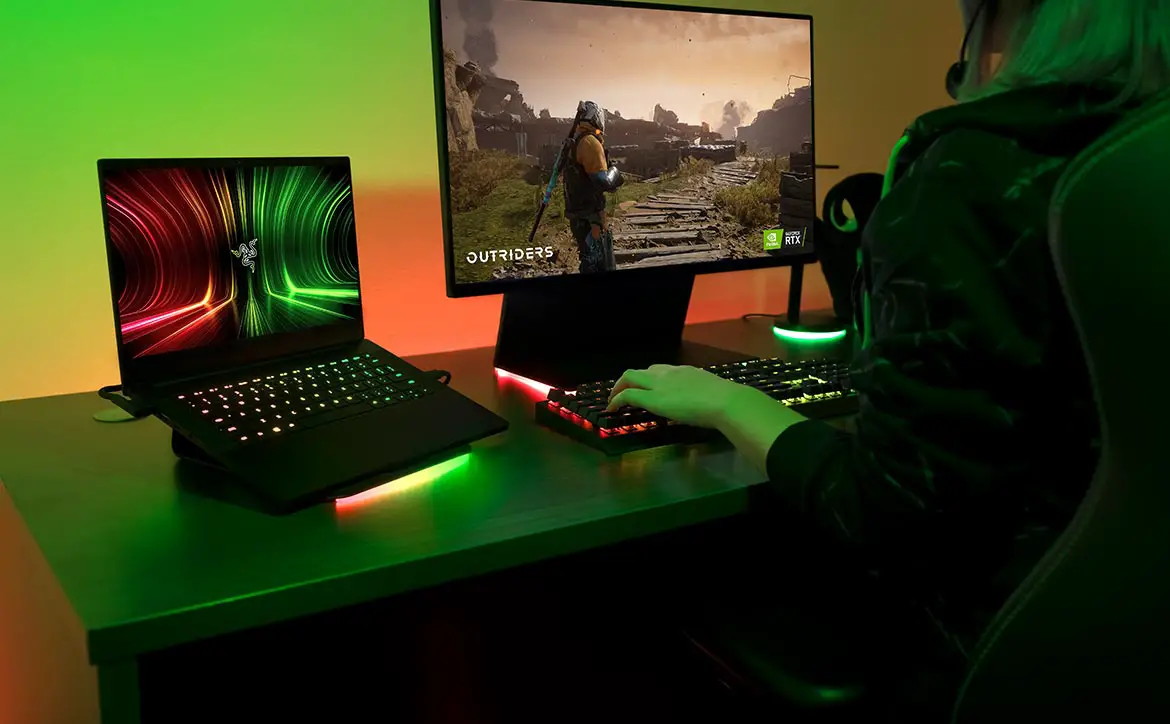 Razer Blade 14 gaming laptop and Razer Raptor 27 gaming monitor on desk with gamer playing Outriders