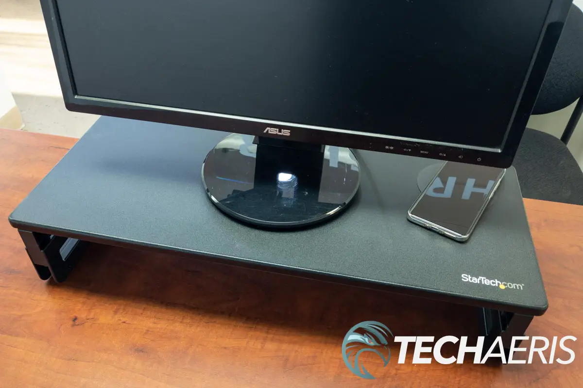 The StarTech Monitor Riser Stand with Wireless Charging Pad with a monitor and smartphone sitting on it