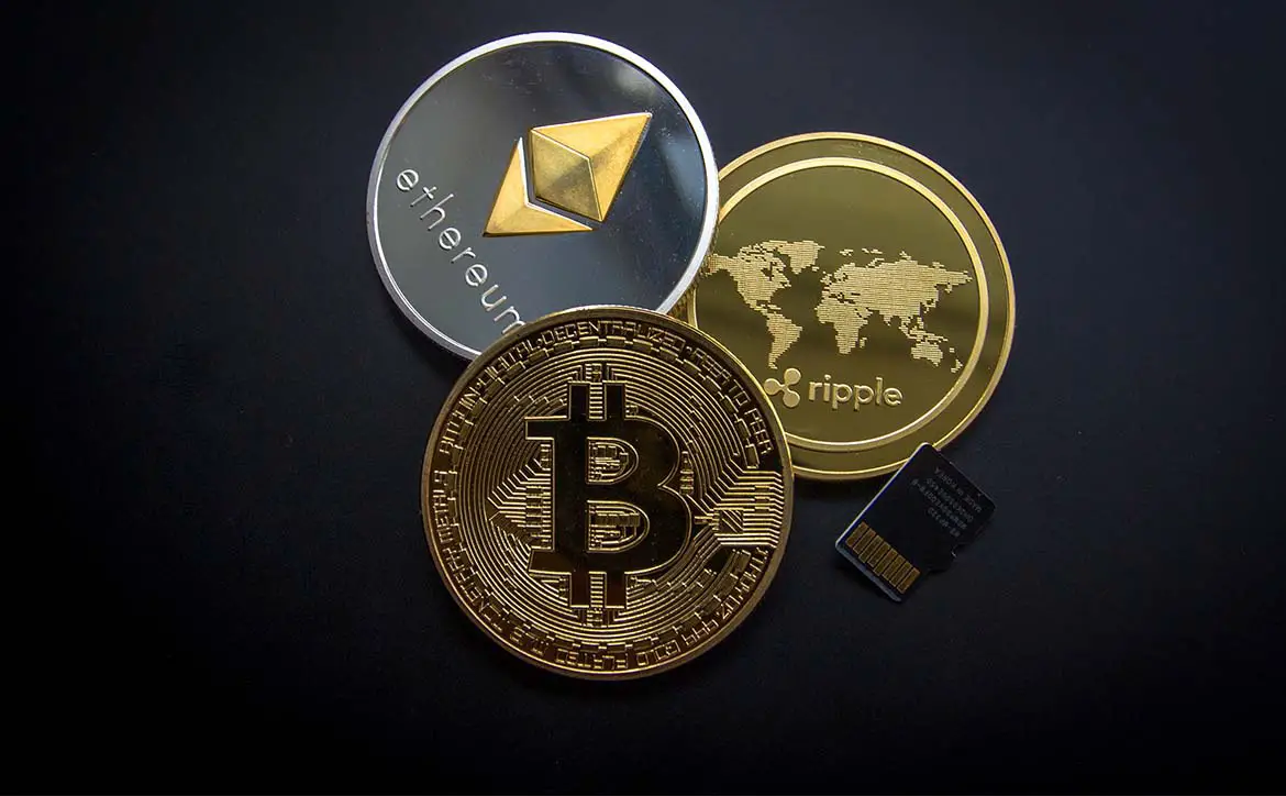 Three cryptocurrency coins including Bitcoin, Ethereum, and Ripple beside a small USB key